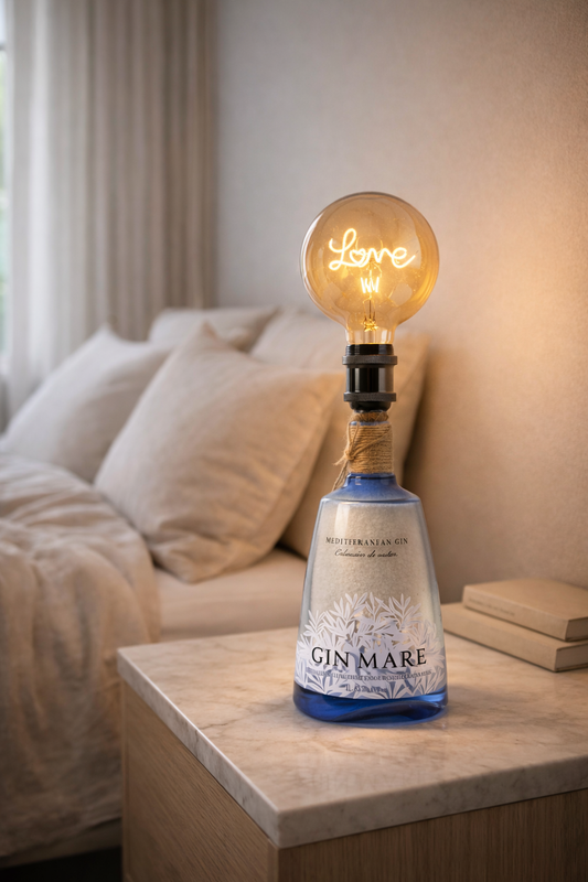 Lampada artigianale Gin Mare con lampadina vintage “Love” accesa su comodino in marmo, in camera da letto moderna con toni beige e atmosfera calda rilassante