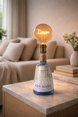 Lampada da tavolo artigianale con bottiglia Gin Mare e lampadina “Dream”, posizionata su mobile in marmo in salotto moderno minimal con luce naturale