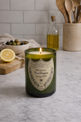 Candela Dom Pérignon riciclata accesa su piano cucina con limone, olive e utensili in legno in ambiente moderno