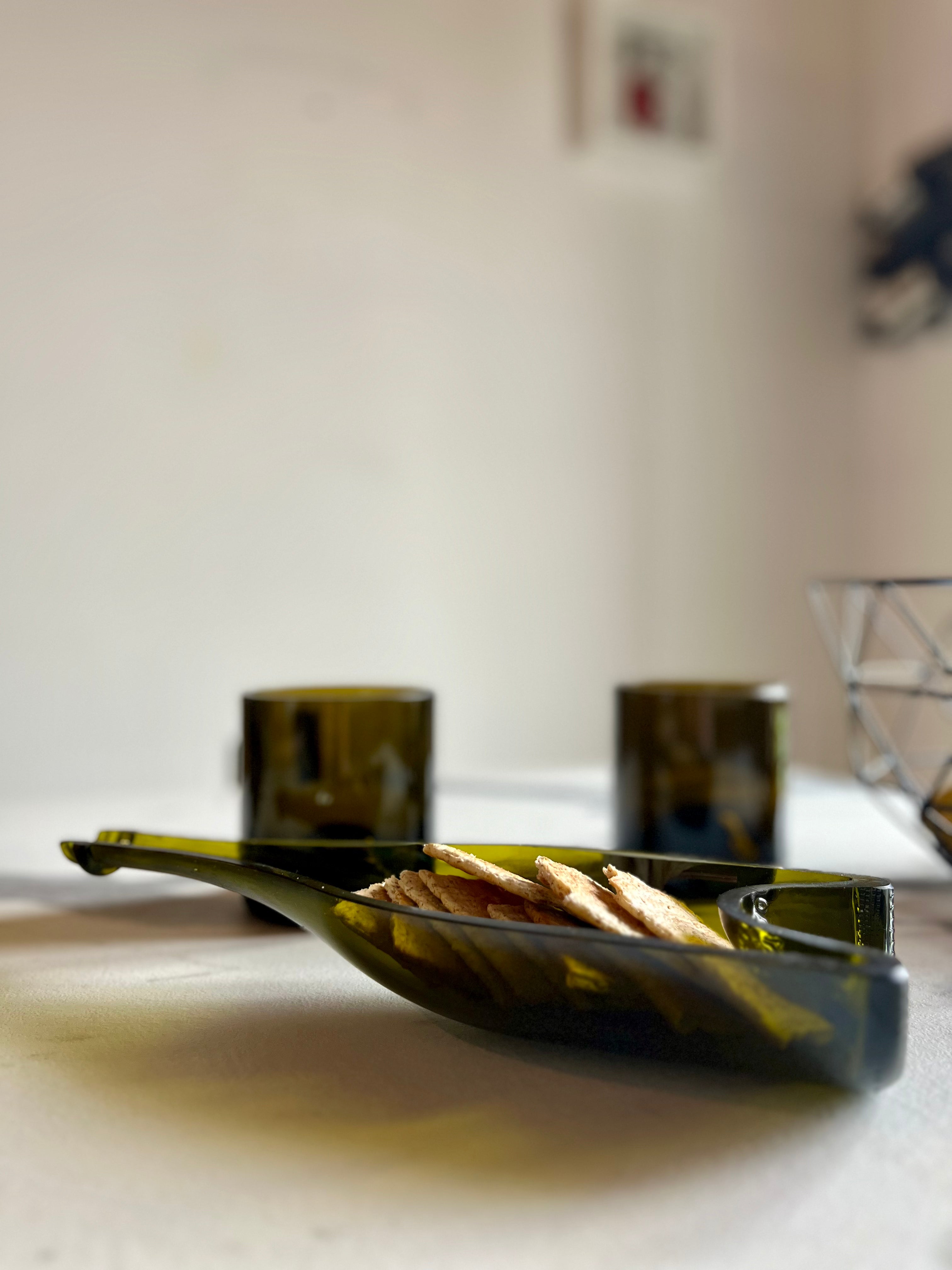 Set aperitivo in vetro riciclato con piatto porta snack e bicchieri visto dall’alto su tavolo elegante