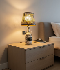 Lampada da tavolo fatta a mano con bottiglia Kraken e paralume nero traforato, accesa su mobile in camera da letto contemporaneo