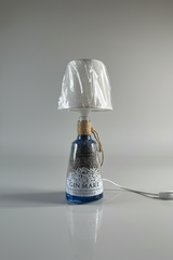 Lampada realizzata con bottiglia di gin mare, con paralume in tessuto beige e corda decorativa, appoggiata su un tavolino in marmo