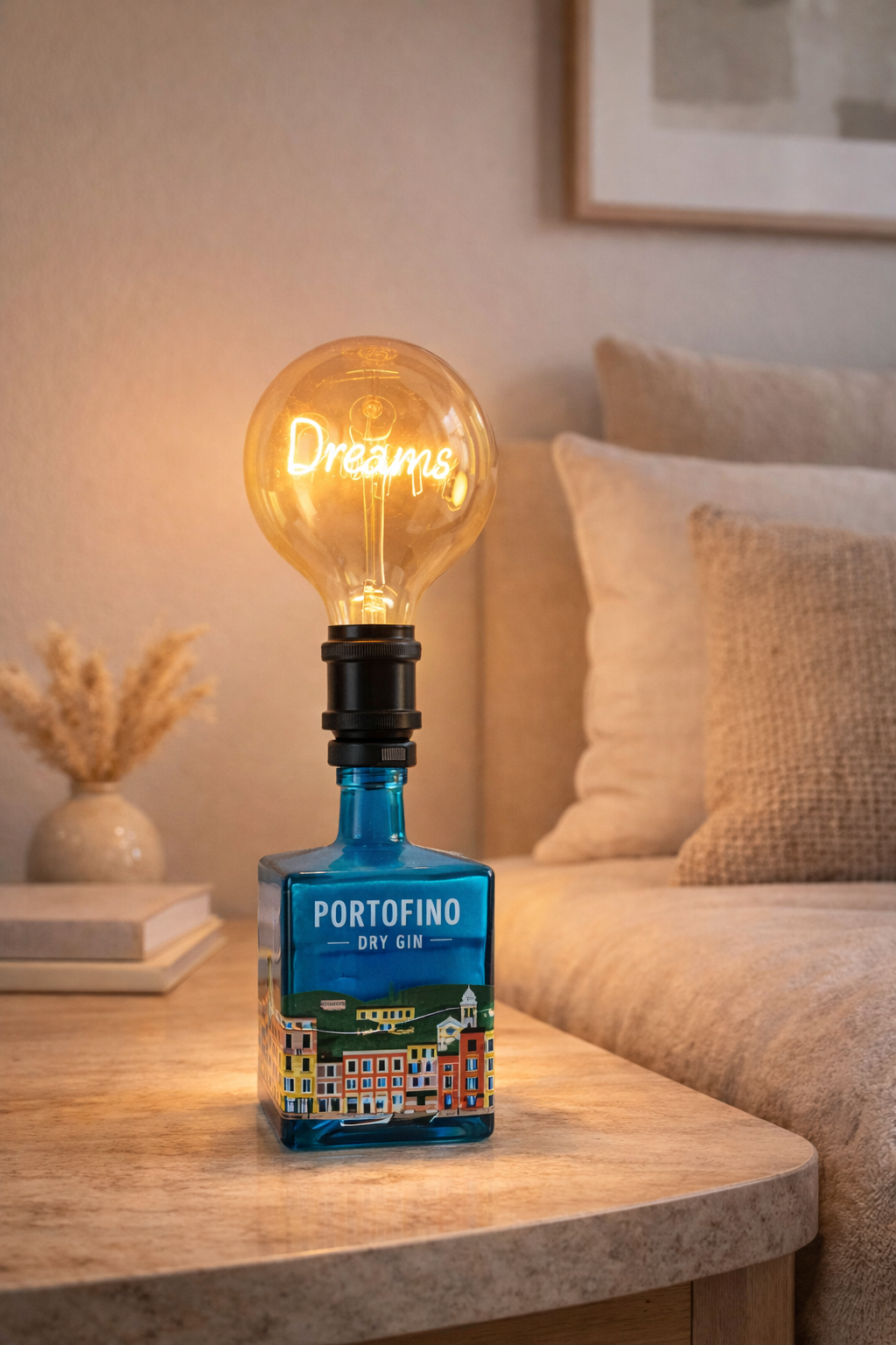 Lampada da tavolo artigianale realizzata con bottiglia di gin Portofino riciclata, con lampadina vintage a luce calda “Dreams”, posizionata su comodino in legno in una camera da letto dai toni neutri e atmosfera accogliente.
