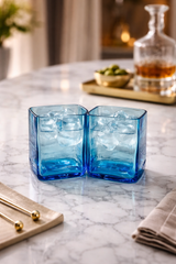 Bicchieri in vetro blu riciclato su superficie chiara con luce naturale in stile minimal ed elegante