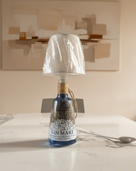 Lampada da tavolo realizzata con bottiglia di gin riciclata, con paralume in tessuto beige e corda decorativa